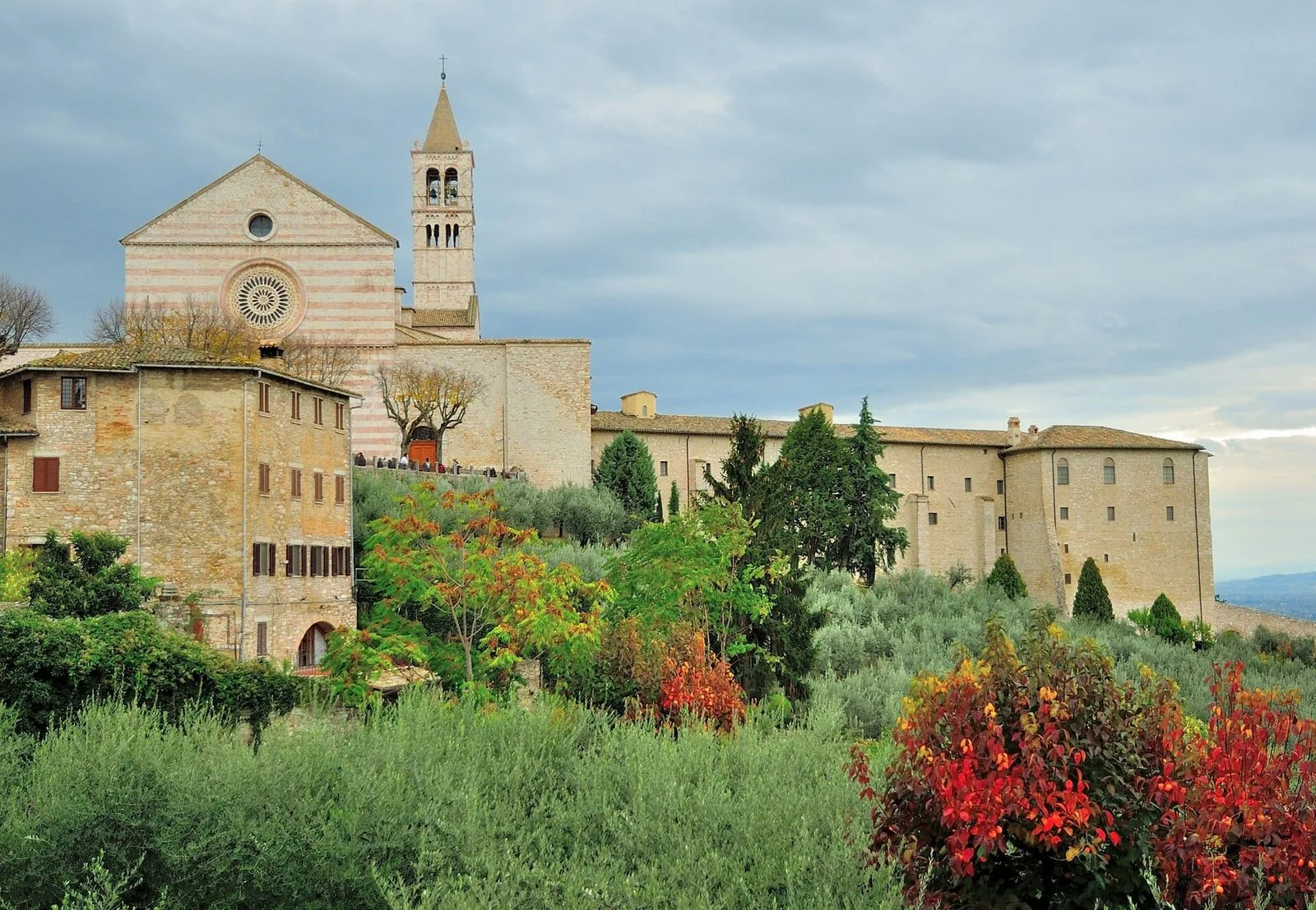 Basilica di Santa Chiara ad Assisi in autunno, con uliveti e arbusti dalle foglie rosse e arancioni in primo piano